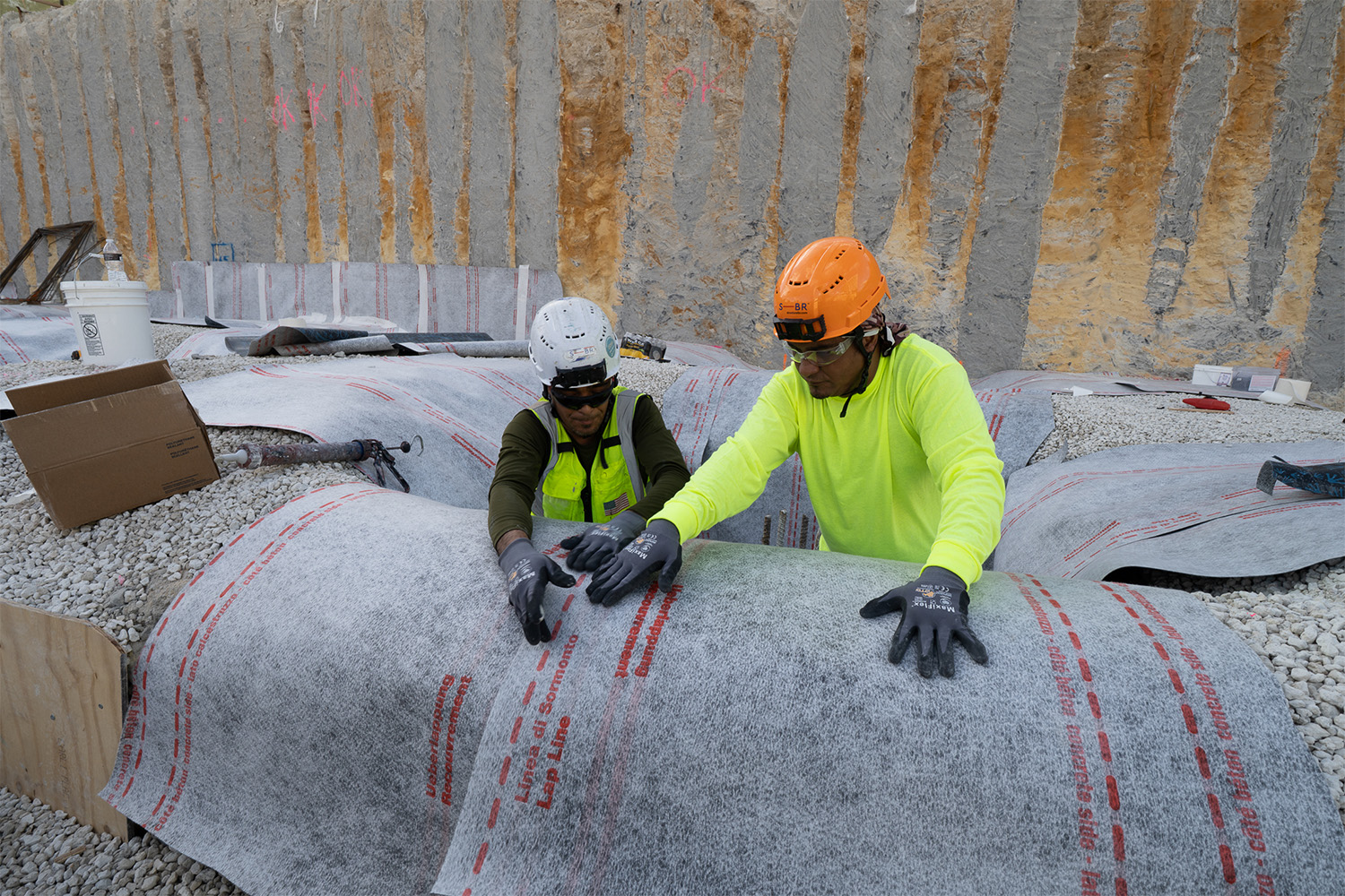 Two workers installing waterproofing in below grade condition.